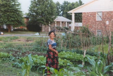 a gardener from southeast Asia stands in her summer garden plot