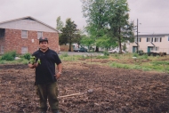 a Latino gardener stands in the newly tilled spring garden holding a transplant