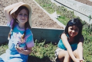 2 young girls sit in front of a raised bed ready to plant