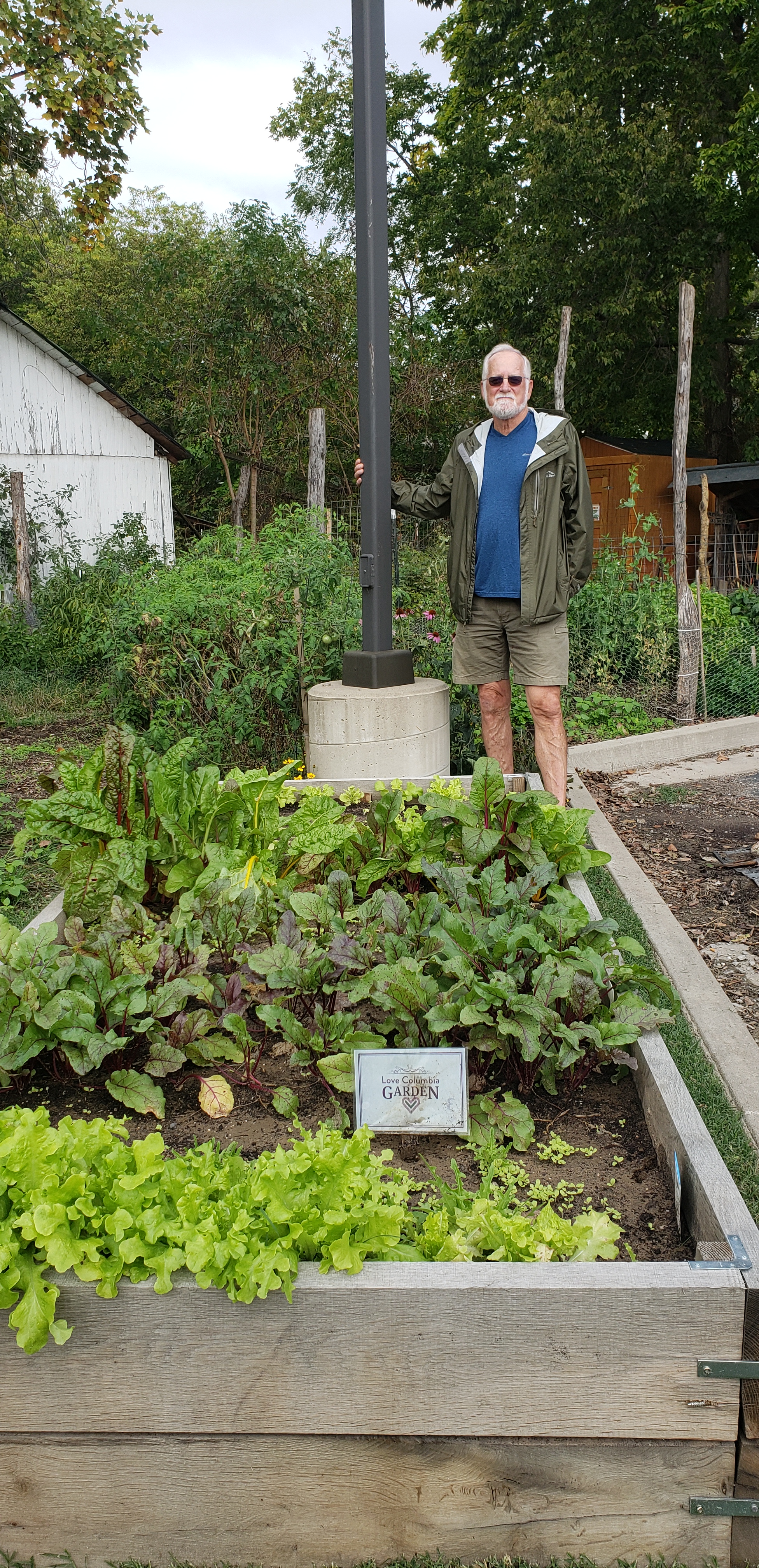 Eric Lorenz stands in front of a raised bed with leafy greens growing in it